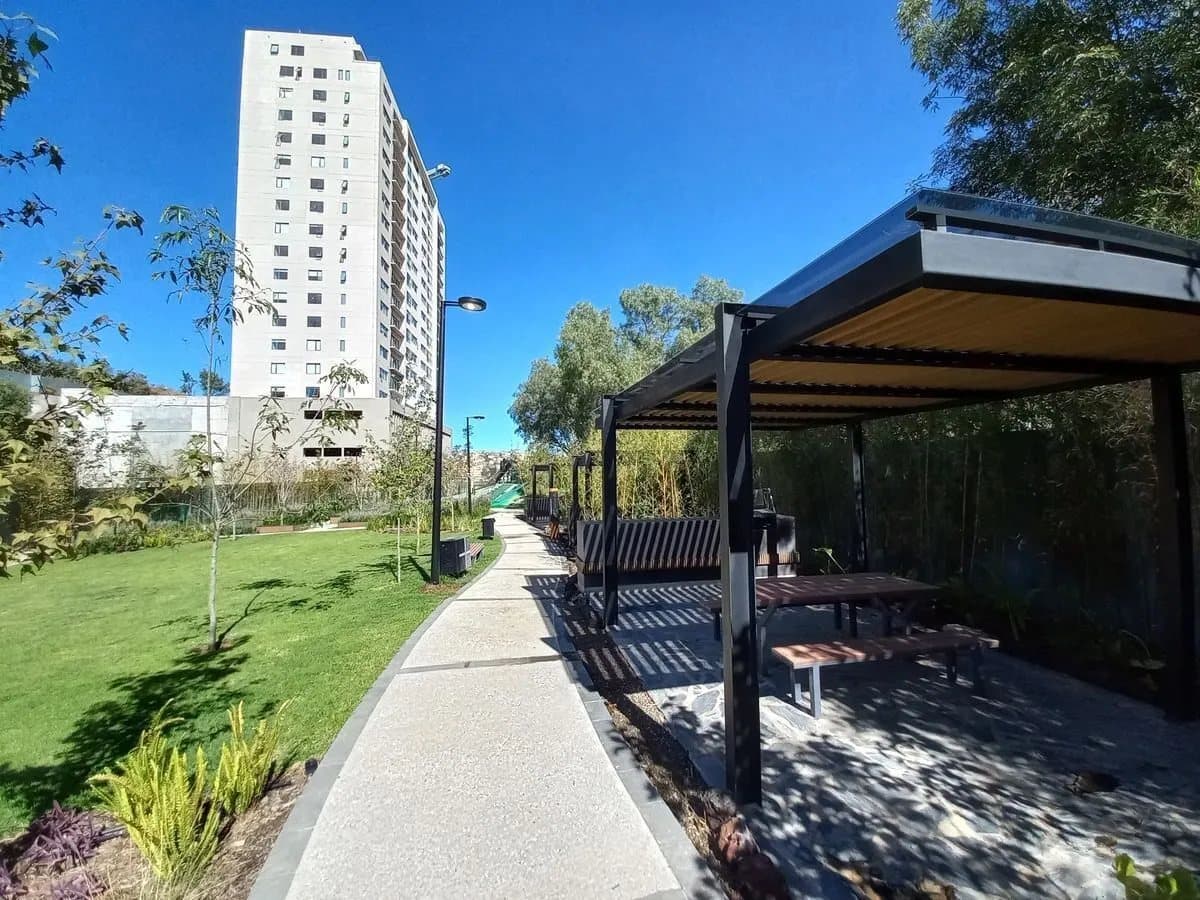 Sendero y pérgolas del parque con una torre al fondo